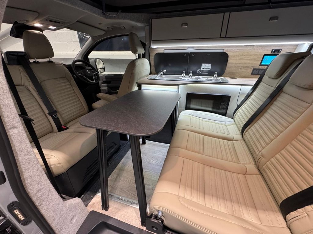 Campervan interior with swivel captain seat, dining table and kitchen